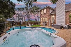 A backyard with a hot tub, a basketball hoop, and a house with a brick exterior. - Grand Gem for Large Groups: Pool, Cinema, Playroom (Carrollton)