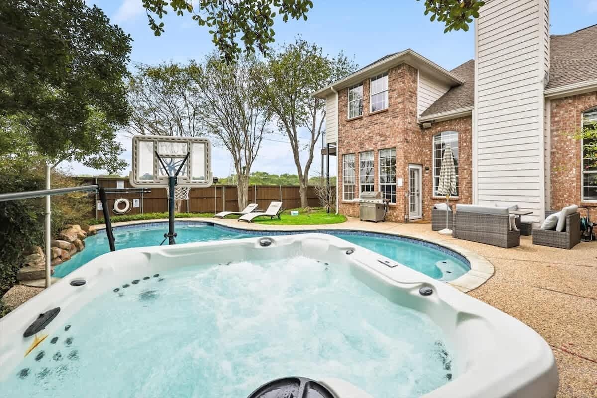 A backyard with a hot tub, a basketball hoop, and a patio area with outdoor furniture.