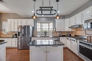 A modern kitchen with white cabinetry, stainless steel appliances, a central island, and pendant lighting. - Grand Gem for Large Groups: Pool, Cinema, Playroom (Carrollton)