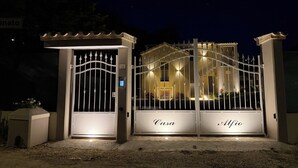 Een hekpoort met borden 'Casa' en 'Alfio', een beveiligingscodeklavier en een goed verlichte gevel in de nacht.
