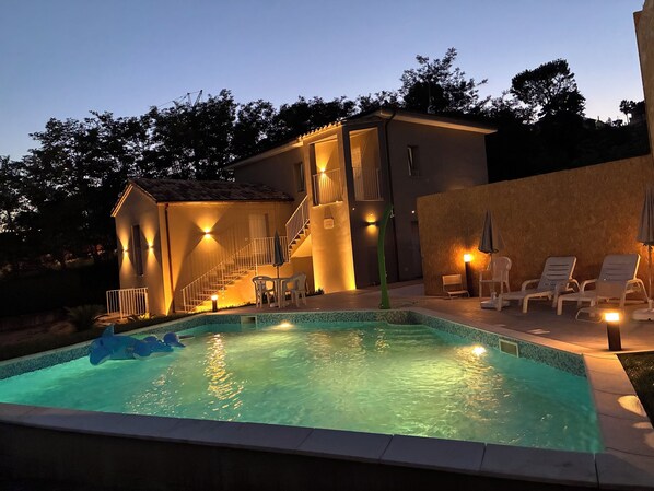A swimming pool with a small boat, a staircase leading to a second floor, and outdoor seating with umbrellas.