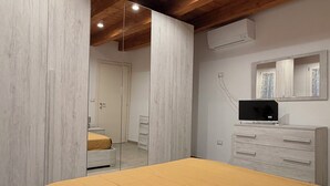 A bedroom with a bed, wooden ceiling beams, a mirror, a dresser, and an air conditioning unit.