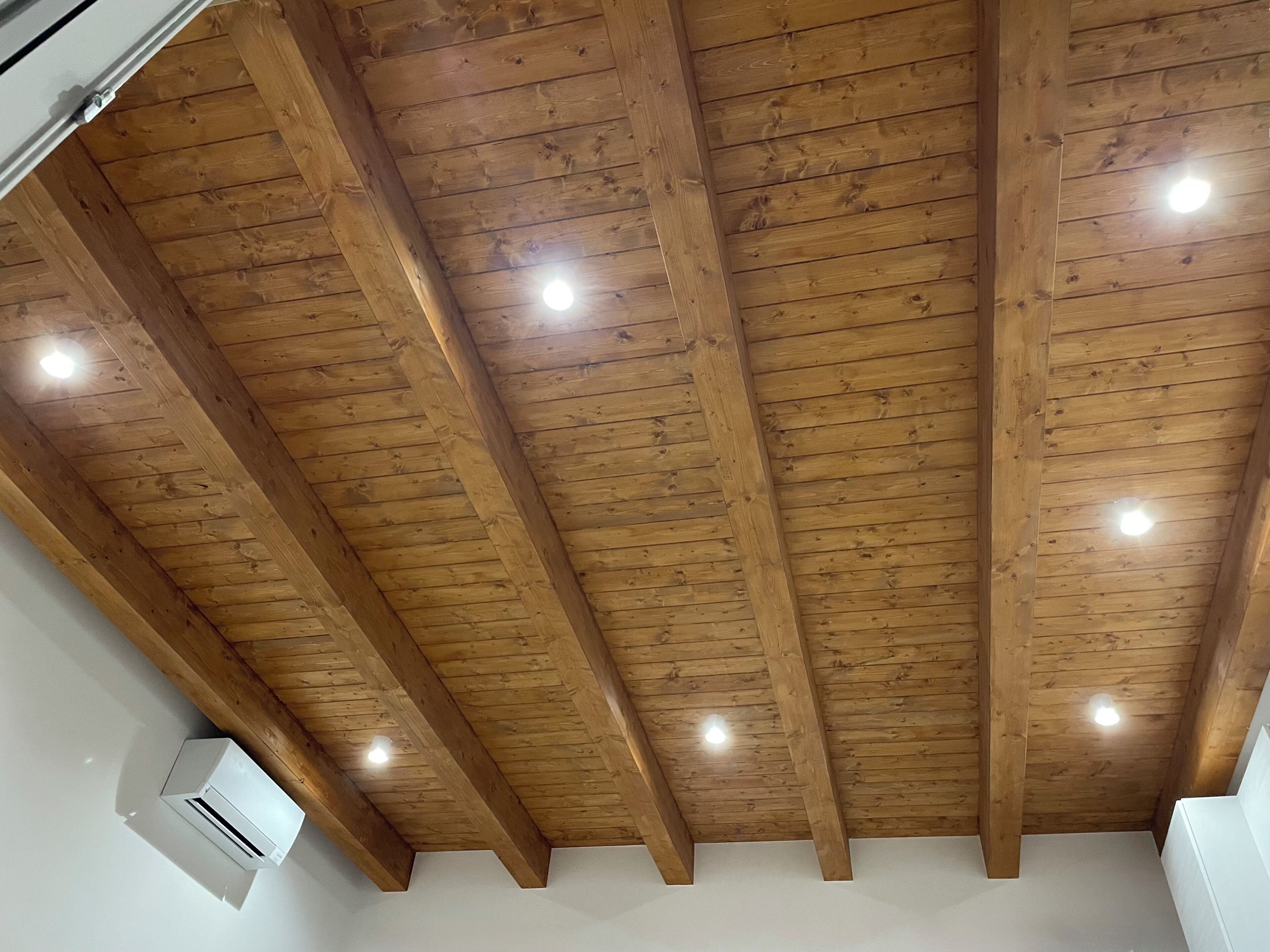 Une pièce avec un plafond en bois, des spots encastrés et un appareil de climatisation blanc.