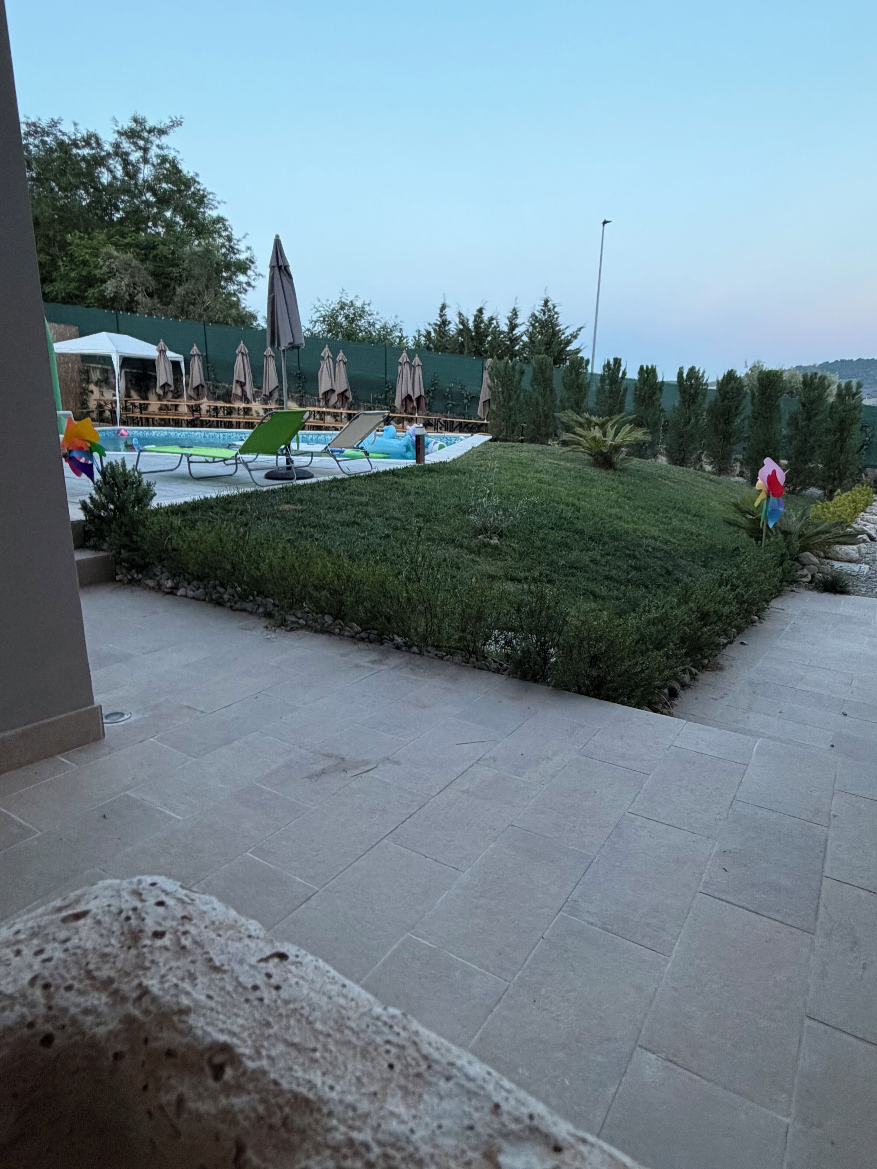 A swimming pool with lounge chairs and umbrellas, surrounded by greenery and a stone pathway.