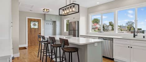 A modern kitchen with a large island, bar stools, stainless steel appliances, and a view of the neighborhood.