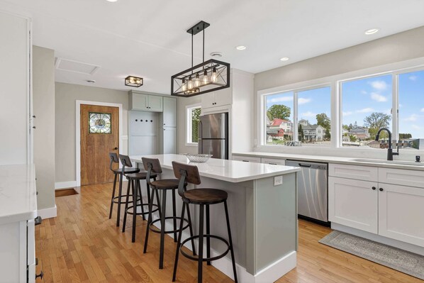 A modern kitchen with a large island, bar stools, stainless steel appliances, and a view of the neighborhood.