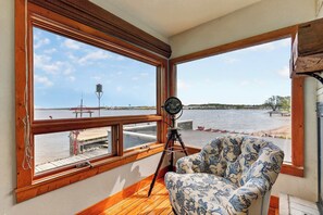A room with large windows, a telescope, and a patterned chair.