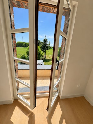 A room with a large window revealing a view of a green field and a tree. - Design green house very central but quiet (Kontich)