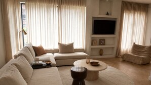 Un salon moderne avec un canapé d’angle, une table basse ronde et un téléviseur à écran plat fixé au mur.