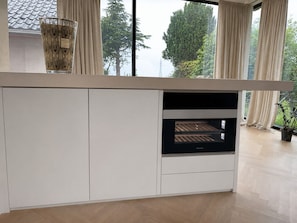 A modern kitchen with a built-in oven, a glass cabinet, and a view of trees through large windows. - Design green house very central but quiet (Kontich)