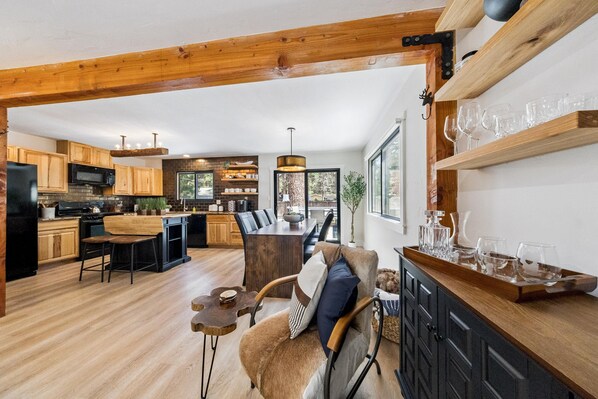 A spacious kitchen with wooden cabinets, a dining area with a wooden table and chairs, and a bar area with a tray of glasses.