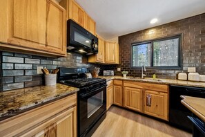 A kitchen with wooden cabinets, a black stove, a microwave, and a brick backsplash.