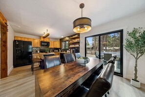 A modern kitchen with wooden cabinets, a black refrigerator, a dining table with chairs, and a large window.