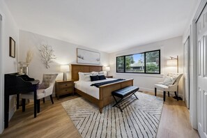 A bedroom with a bed, bedside tables, a desk, a chair, a window, and a view of the outdoors.
