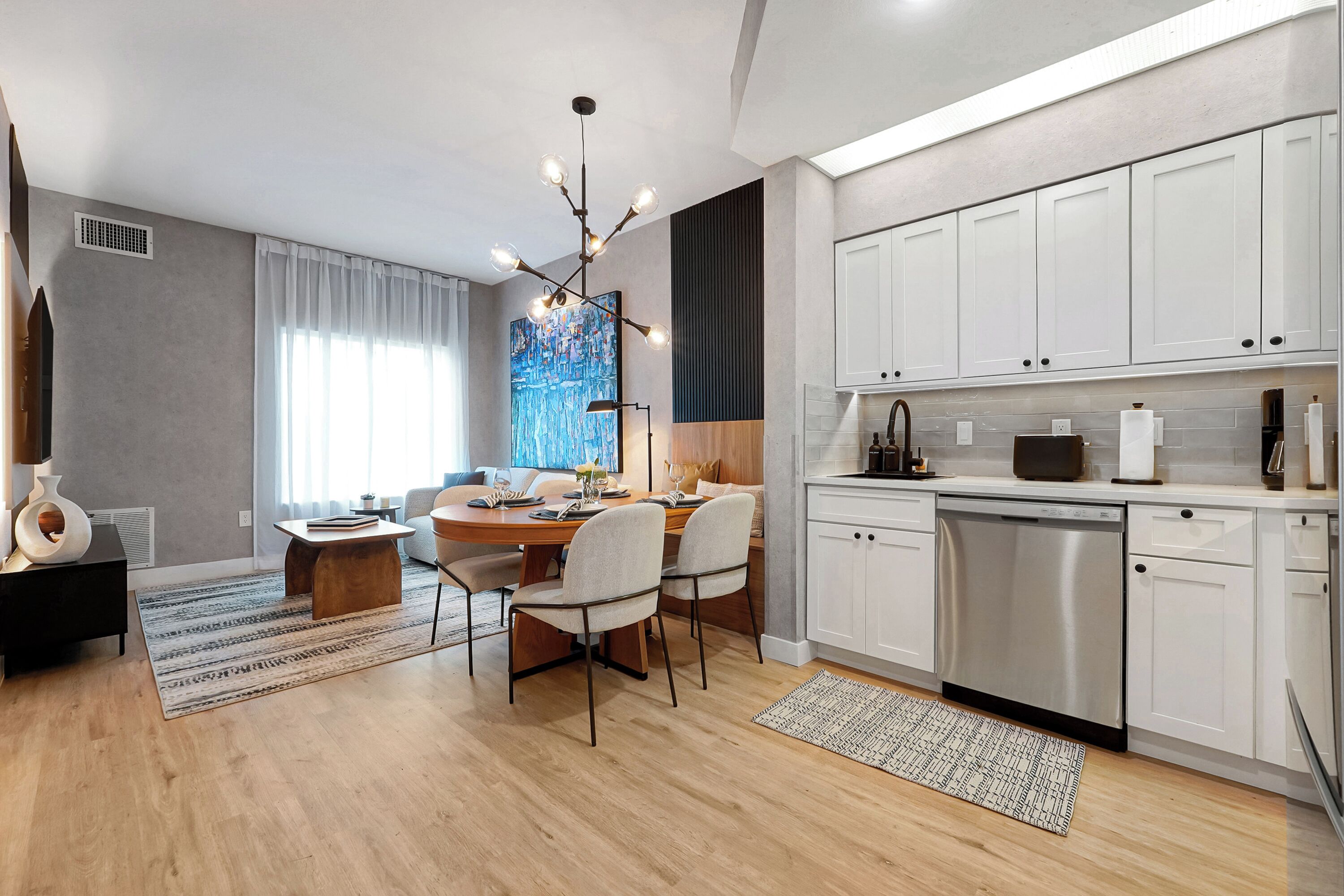 A modern kitchen with white cabinets, a dishwasher, and a dining area with a table and chairs.