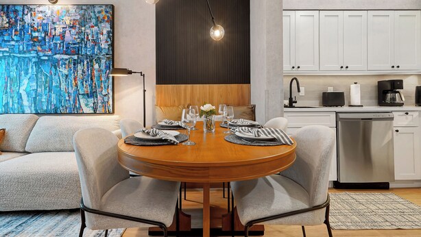 A modern dining area with a round table, grey upholstered chairs, and a wooden floor. - 1 bedroom apartment near Disney and Universal (Orlando)