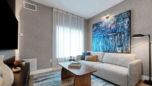 A modern living room with a sofa, a coffee table, a large abstract painting, and a floor lamp. - 1 bedroom apartment near Disney and Universal (Orlando)