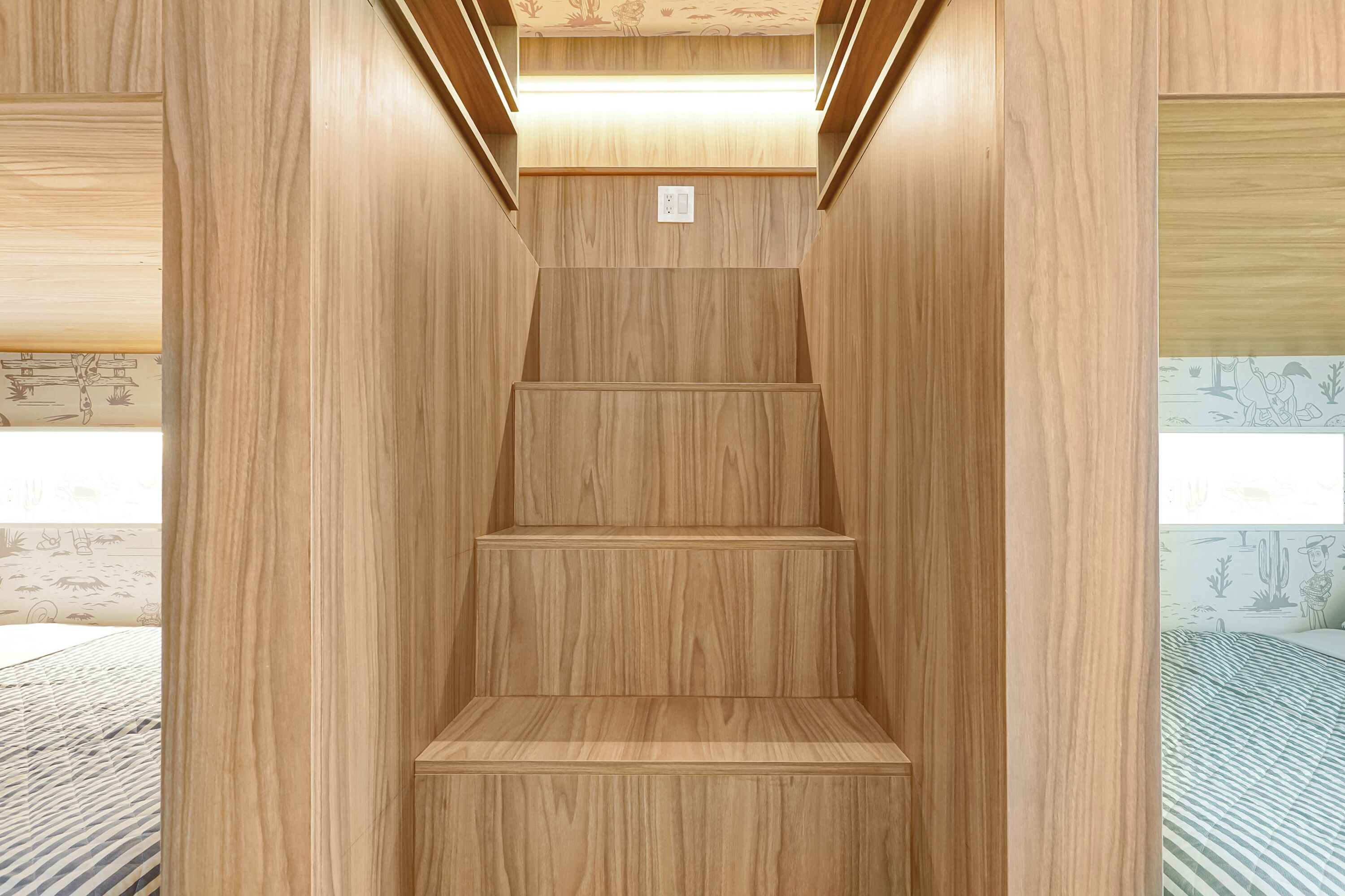 Una escalera de madera en una habitación con papel tapiz estampado y una cama a rayas.