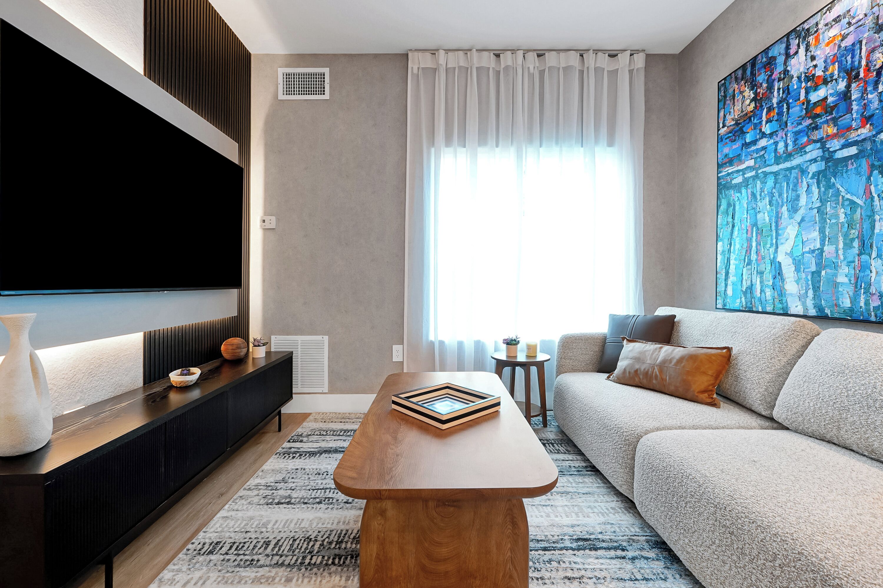 A modern living room with a flat-screen TV, a wooden coffee table, a sofa, and a large abstract painting.