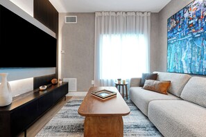 Ein modernes Wohnzimmer mit einem Flachbildfernseher, einem Holztisch, einer Couch und einem großen abstrakten Gemälde.