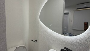 Une salle de bain avec des toilettes blanches, un lavabo doté d’un robinet noir et un miroir placé devant un mur à texture.