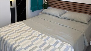 Une chambre à coucher avec un lit, un tableau, une table de chevet, une serviette verte et un mur orné d’un luminaire circulaire.