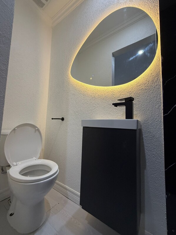 Un bagno con il water bianco, un lavandino nero e uno specchio con illuminazione circolare.
