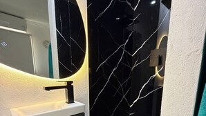 Une salle de bain moderne avec un mur en marbre noir, un lavabo blanc et un miroir doté d’un cadre circulaire.
