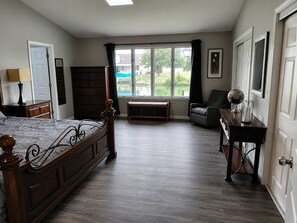 A bedroom with a large bed, a chair, a desk, and a window with a view of greenery. - Spacious 6 bedroom, 5 bathroom, and 2 game room house on Grand Lake! (Saint Marys)