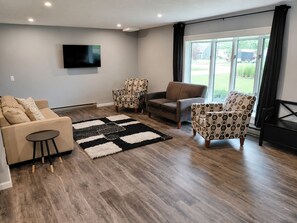 A modern living room with a large window, a flat-screen TV, and a patterned rug. - Spacious 6 bedroom, 5 bathroom, and 2 game room house on Grand Lake! (Saint Marys)
