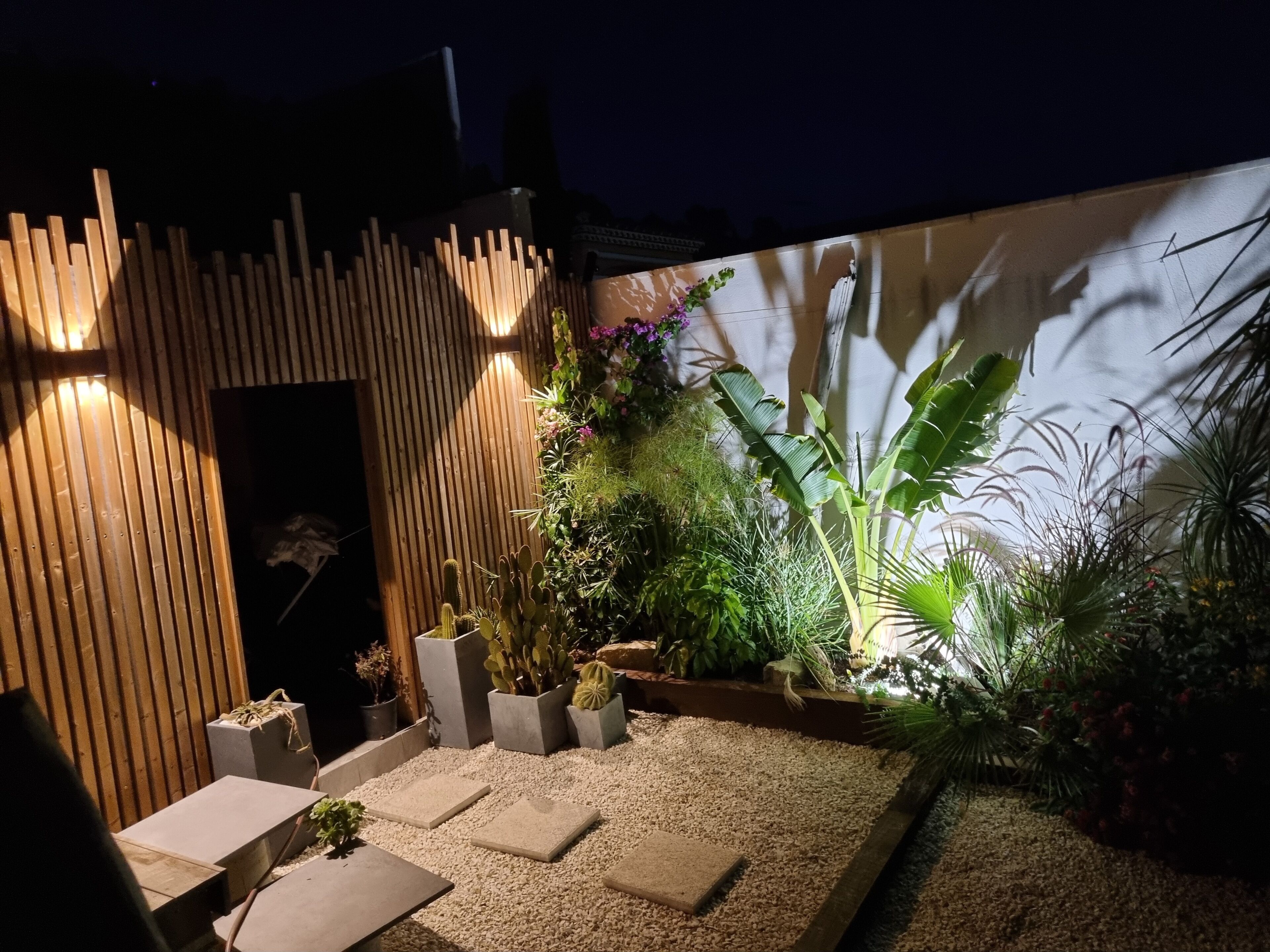 A garden with a wooden structure, potted plants, and a gravel pathway.
