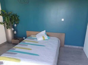 A bedroom with a bed, a nightstand, a lamp, and a potted plant. - Vrbo Property (Calvisson)