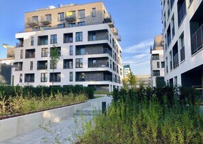 A modern multi-story residential building with balconies, a paved walkway, and greenery. - Sweet Place Apart (Poznań)