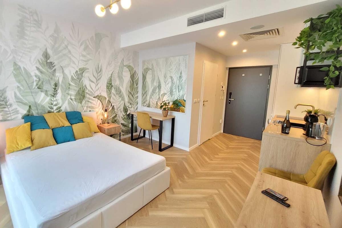 A modern bedroom with a large bed, a desk, and a kitchenette.