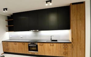 A modern kitchen with black cabinets, wooden lower cabinets, a built-in oven, and a stainless steel countertop.