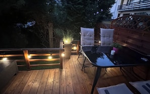 A wooden deck with a table and chairs, surrounded by a wooden fence and trees.