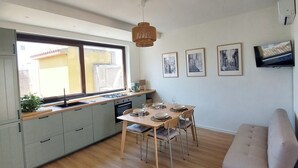 A modern kitchen with a dining area, wooden flooring, and a sofa.