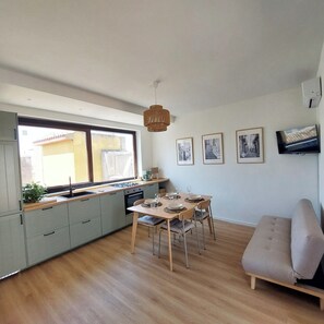 A modern kitchen with a dining area, wooden flooring, and a sofa.