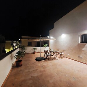 Una terraza en la azotea con mesa y sillas, plantas en macetas y una pérgola.