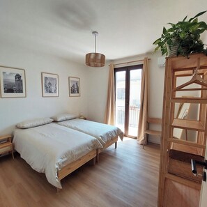 Un dormitorio con dos camas, una lámpara colgante, una puerta de balcón y cuadros en la pared.
