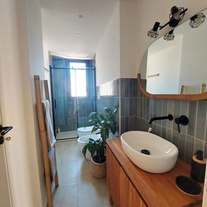 Un baño moderno con un espejo grande, lavamanos blanco y zona de ducha.
