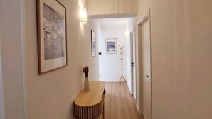 A hallway with a wooden floor, a table with a vase, and framed pictures on the walls.