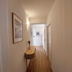 A hallway with a wooden floor, a table with a vase, and framed pictures on the walls.