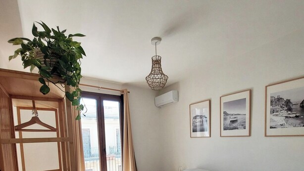 A bedroom with a bed, a wooden wardrobe, a hanging plant, and three framed pictures on the wall.