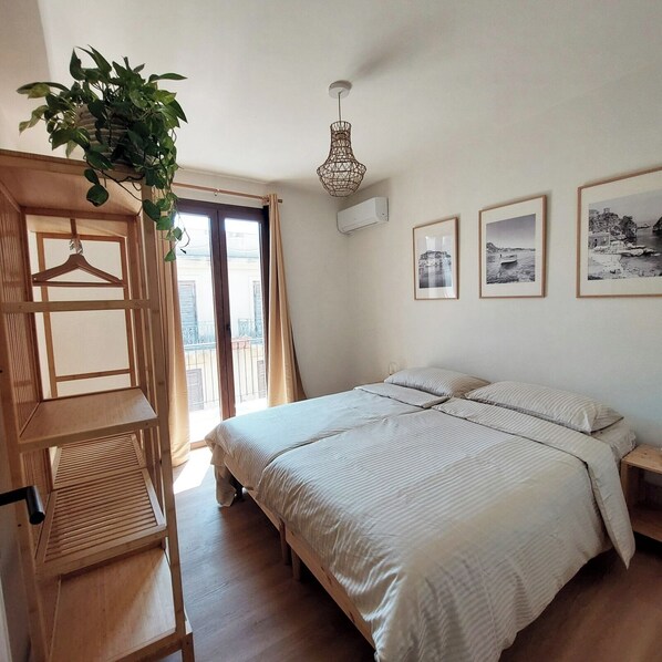 A bedroom with a bed, a wooden wardrobe, a hanging plant, and three framed pictures on the wall.