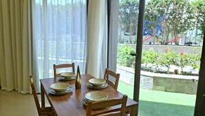 A dining table with chairs and plates, a window with curtains, and a view of a garden and buildings outside.