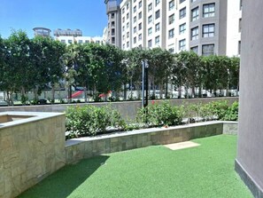 A courtyard with artificial grass, stone planters, and a building in the background.