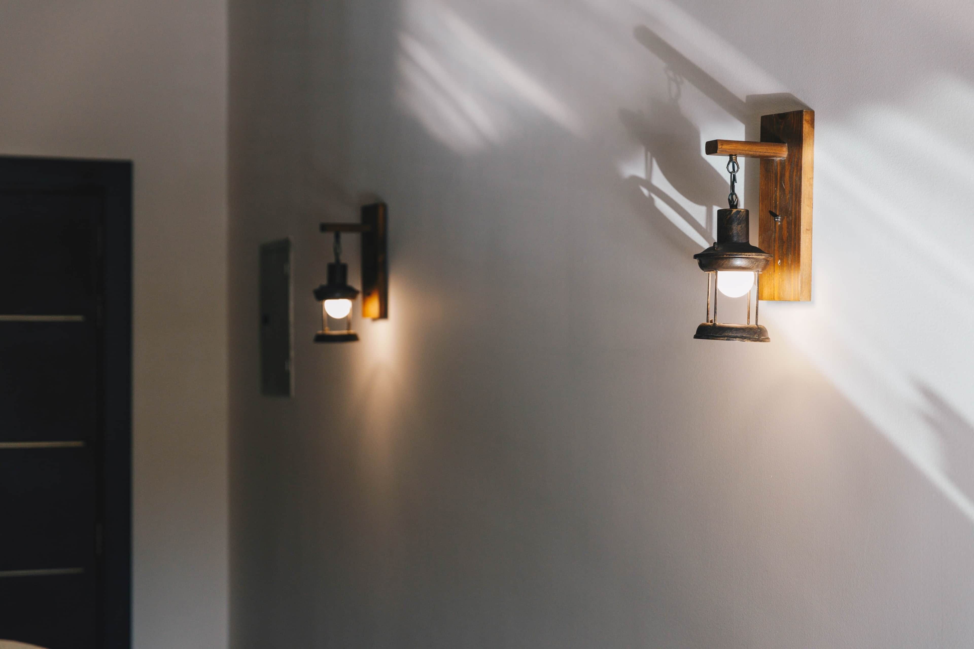 Two wall-mounted light fixtures with exposed bulbs, a wooden door frame, and a plain wall.