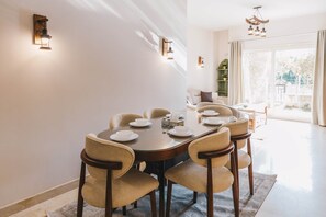 A dining area with a round table, six chairs, and wall-mounted light fixtures. - The Suite, Palm Hills - V702 (New Cairo City)