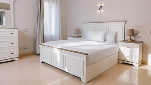 A bedroom with a large bed, bedside tables, a dresser, and a window with curtains. - The Suite, Palm Hills - V702 (New Cairo City)